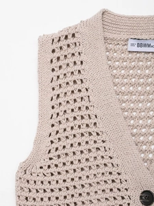 Detailed macro view of apricot hollow-out knit vest with handmade crochet patterns and buttons