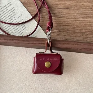 Close-up of a mini burgundy leather bag pendant with gold hardware and woven lanyard