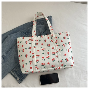 Flat lay of cream cherry print tote bag with phone for size reference and denim jacket