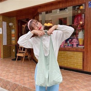 Detail of mint green canvas tote bag with knot design carried by model in casual scene