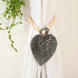 Close-up of handcrafted cotton rope curtain tieback with wooden beads and gray woven leaf
