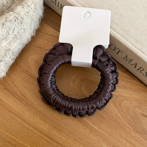 Détail d'un chouchou plissé marron foncé avec une texture satinée soyeuse sur la table