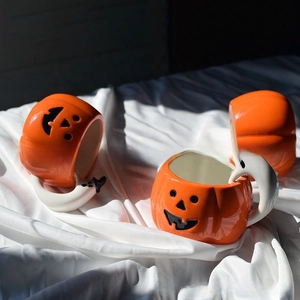 Detail of orange pumpkin ceramic mugs with white ghost handle on silk fabric