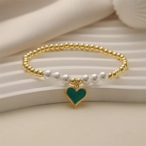Elegantes Goldperlenarmband mit weißen Perlen und grünem Herzanhänger auf gewellter Basis