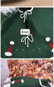 Close-up of green knit Christmas tree skirt with white bows and Santa hat embroidery
