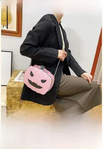 Pink pumpkin crossbody bag with black face pattern and metal chain detail on model