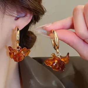 Vintage gold hoop earrings with amber flower petals on dark brown leather texture