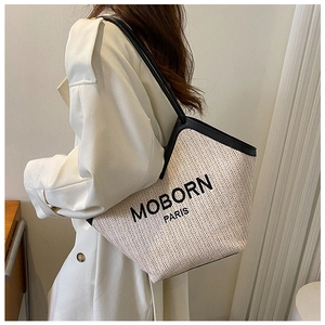 Detail of woven straw tote bag featuring MOBORN PARIS logo and black leather straps