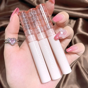 Close-up of three glossy mirror finish lip glazes held by a hand over silk fabric