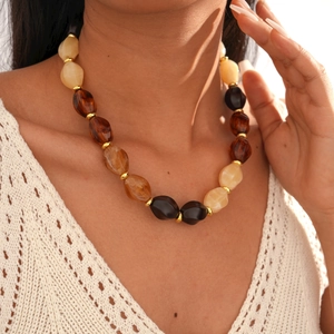 Detailed close-up of acrylic oval beaded necklace in amber and cream with gold spacers