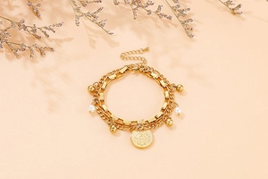 Detail of double-layer gold chain bracelet with Hamsa Hand coin and faux pearls