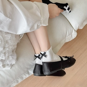 Close-up of white Lolita style cotton socks with ruffled edges and black ribbon bows