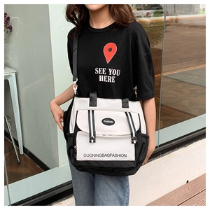 Detail of a large black and white canvas messenger bag with FASHION logo and shoulder strap