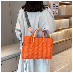 Detail of orange quilted tote bag featuring pink handles and a blue patterned strap