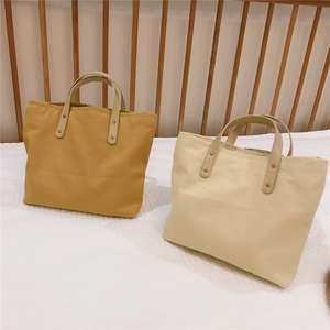 Detail of canvas tote bags in yellow and beige with faux leather handles and metal rivets
