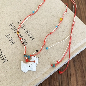 Detail of woven rope necklace featuring a white resin dog pendant and colorful beads