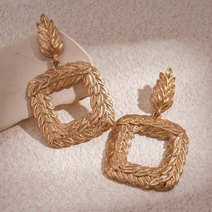 Golden geometric square earrings with wheat ear embossing on stone background