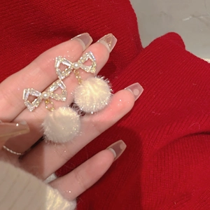 Detailed close-up of bow knot earrings featuring white plush pompom and sparkling crystals