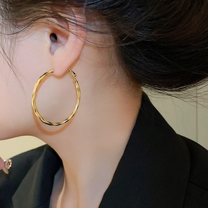 Macro detail of large twisted 14k gold plated hoop earrings showing hammered texture