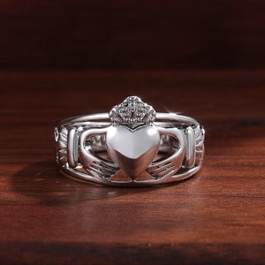 Gros plan d'une bague Claddagh en argent avec deux mains tenant un cœur couronné