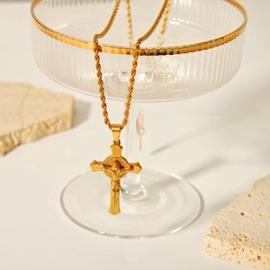 Pendentif crucifix doré élégant avec chaîne torsadée présenté sur bord en verre