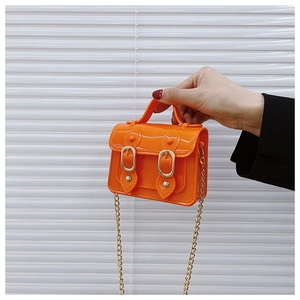 Detail of orange jelly mini bag with golden chain strap and magnetic buckles shown by hand