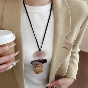 Detail of a three-layer geometric resin pendant necklace on a leather cord over a white top