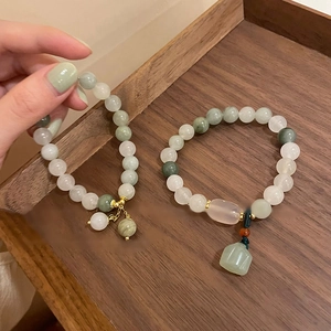 Close-up of green and white jade beaded bracelet with a lotus pendant on wood