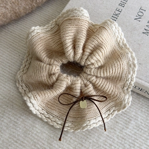 Detail of beige knit scrunchie with cream lace edge, brown bow and gold handmade tag