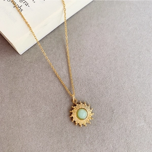 Détail d'un pendentif soleil vintage doré avec pierre verte sur fond texturé