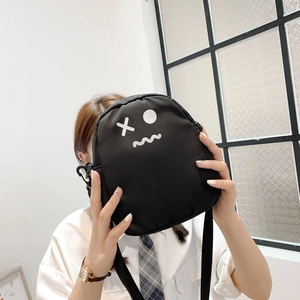 Détail du sac bandoulière en toile noire avec imprimé visage cartoon blanc et sangle
