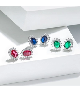 Close-up of sapphire, emerald, and ruby oval stud earrings with halo diamond setting