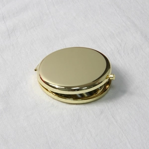 Detailed view of a gold circular folding makeup mirror on a white linen texture background