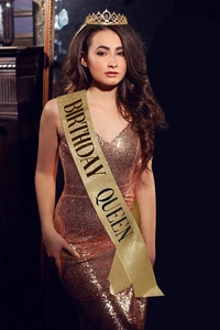 Close-up of sparkling gold Birthday Queen sash worn by an elegant model in a gown