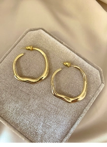 Detailed view of irregular gold circular earrings on a beige velvet display pad
