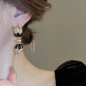 Close-up of retro gold-plated drop earrings with zircon and black enamel on model