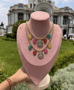 Detail of colorful enamel Virgin Mary pendants and gold beaded chain on pink velvet stand