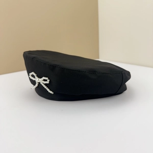 Detail of a black beret featuring a delicate white faux pearl bow ornament on the side