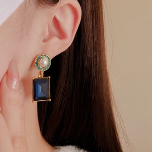 Close-up of vintage gold earrings with deep blue square rhinestones on a model