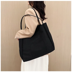 Detailed view of a large black canvas tote bag worn by a model in a camel blazer