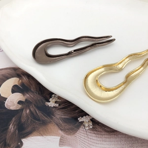 Minimalist U-shaped metal hair pins in gold and gun grey finish on a ceramic plate