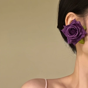 Detailed side view of a large purple fabric rose earring worn on an ear profile.