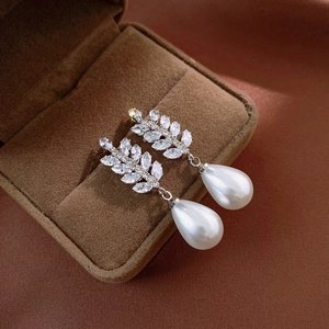 Macro shot of silver wheat leaf earrings with sparkling zircon and teardrop faux pearls