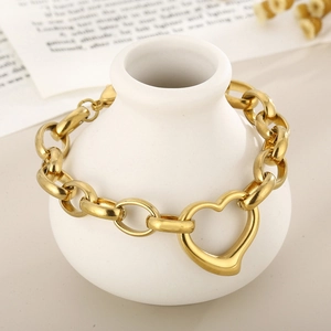 Detailed view of a gold chunky chain bracelet with a heart pendant on a white vase