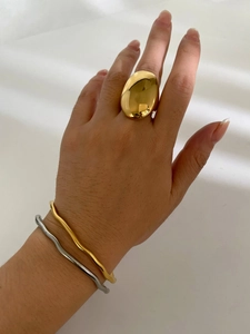 Close-up of model wearing chunky gold oval ring and wavy metallic bangles on white fabric