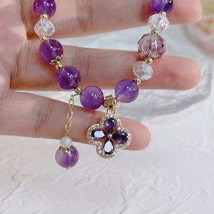 Detail of beaded bracelet with purple amethyst stones and gold four-leaf clover charm