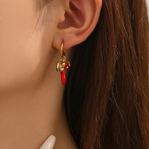Close-up of gold hoop earrings with red chili pendants and butterfly beads on a model