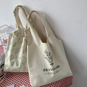 Detailed view of cream canvas tote bags with green leaf patterns on a checkered tablecloth
