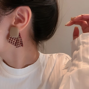 Detail of red and beige houndstooth fabric earring worn on ear with square stud