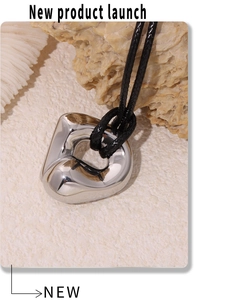 Macro detail of a polished silver heart pendant on a minimalist black cord necklace